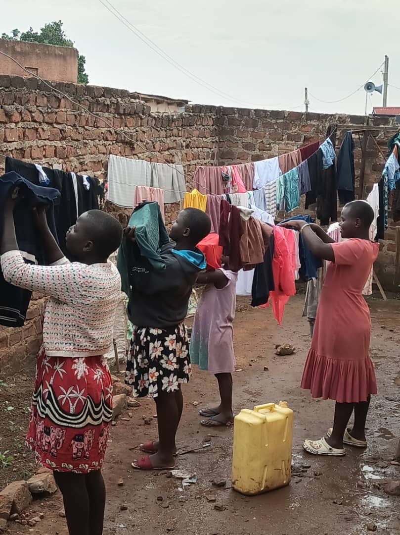 Children hanging laundry in the yard of the rented Love Uganda Foundation home